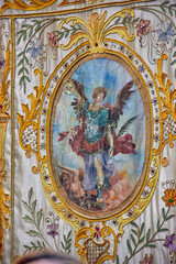 Close-up of an embroidered banner depicting Archangel Michael, carried during the Virgen del Rosario procession in Granada. Religious artwork.