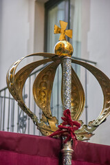 A close-up of a golden crown with a cross on top during the Virgen del Rosario procession in Granada, showing fine details and reflections. Religious art.