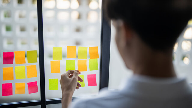 Man organizing project tasks Colorful sticky notes on glass of meeting room