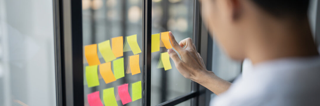 Man organizing project tasks Colorful sticky notes on glass of meeting room - Powered by Adobe