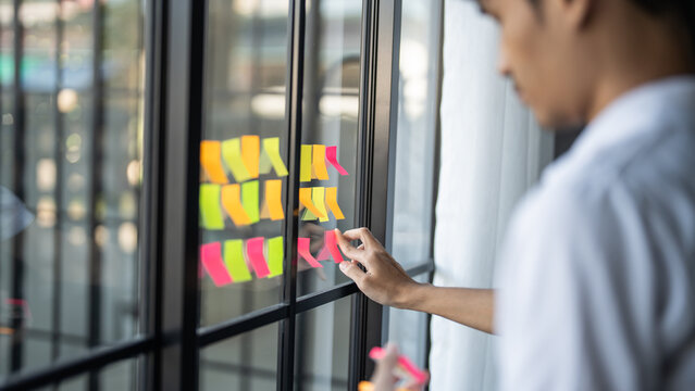 Man organizing project tasks Colorful sticky notes on glass of meeting room