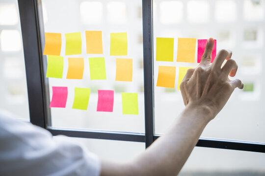 Man organizing project tasks Colorful sticky notes on glass of meeting room - Powered by Adobe