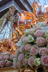 Bouquet of pale pink roses and white lilies in front of glowing candles and a statue of the Virgin Mary during a religious procession. Granada, devotion