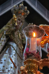 Lit candle with rose petals in a glass holder, glowing in front of the Virgen del Rosario during a night procession in Granada. devotion, tradition