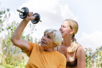 Older woman doing strength training with caregiver support outdoors