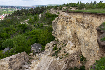 Landslide reveals rocky cliff edge overlooking a green valley under a bright sky during daytime