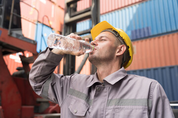 Male worker drinking water from plastic bottle at container yard. Male worker resting and break time at work