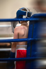 Corner of the boxing ring with a fighter behind blue ropes, resting between rounds. Soft blur enhances the sense of motion.