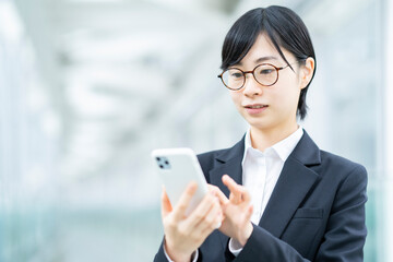 Obraz premium スマートフォンを操作するスーツ姿の若い女性