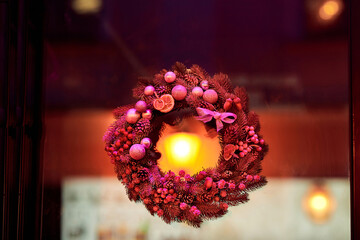 Seasonal christmas wreath with berries and pink baubles glowing warmly in red light festive decoration for holiday home exterior creating cozy inviting atmosphere