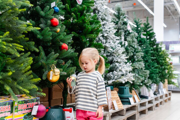 Little child girl shopping in a store with Christmas trees and decorations. Saint Petersburg,...