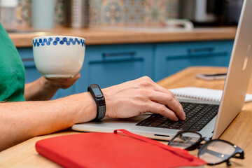 A young man works from home in the kitchen using a laptop. Freelancer working from home