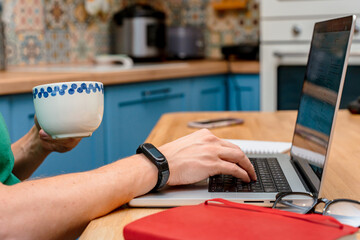 A young man works from home in the kitchen using a laptop. Freelancer working from home