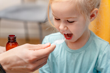 Father gives medicine syrup in a measuring spoon to his daughter little child home