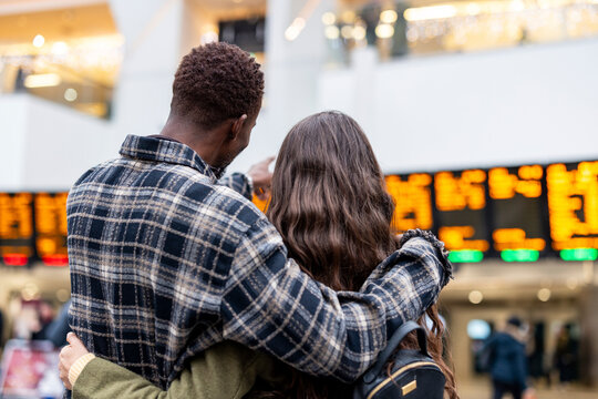 Couple embracing and looking at airport departure board while traveling