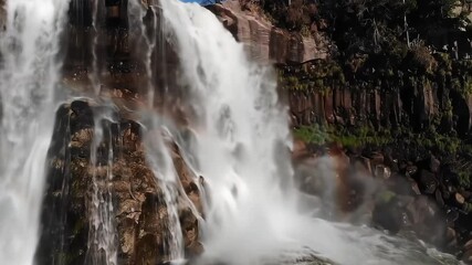 Powerful Waterfall Cascading Down Rocky Cliff Face in Lush Green Landscape on a Bright Sunny Day Creating Mist and Spray in a Natural Environment.