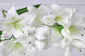 Bright white lilies surround a small glass jar of cream on a reflective surface, creating a calm and elegant atmosphere perfect for showcasing skincare products and beauty rituals