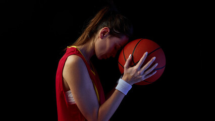 Obraz premium Female basketball player resting forehead on ball in emotional reflection. Concept of inner strength, healing, and balance for sports health and motivation media.