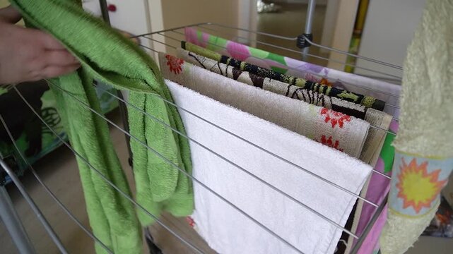 Drying towels on a folding dryer. A hand hangs and adjusts a colored terry towel, home decor, close-up, soft light.