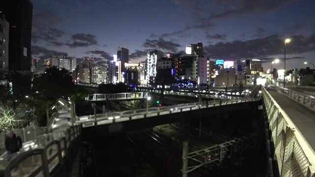 TOKYO, JAPAN - AUG 2025 : Time lapse of Tokyo street near Ikebukuro station from sunset to night. Trains, vehicles, pedestrians and changing city lights. Japanese city life and transportation concept.
