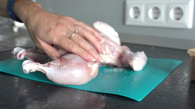 Chicken meat. An unknown woman sprinkles a cut-up chicken with salt. Dietary meat.