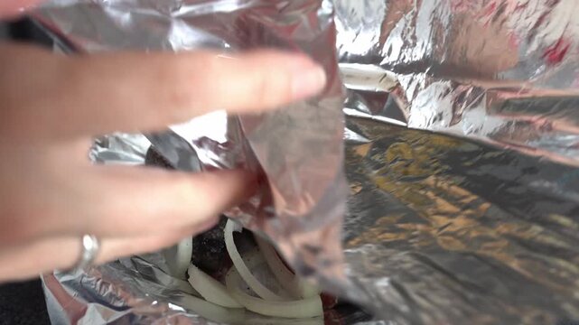 A woman's hands cover a baking dish with foil. She prepares fish for baking in the oven.