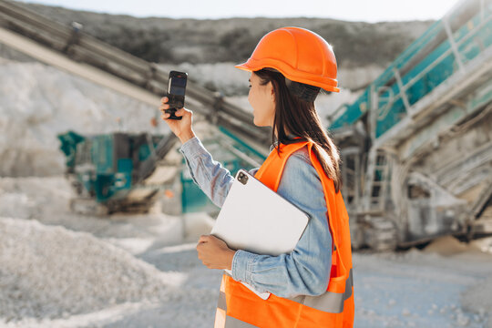 Young woman engineer wearing safety helmet and reflective vest taking photo with smartphone - Powered by Adobe