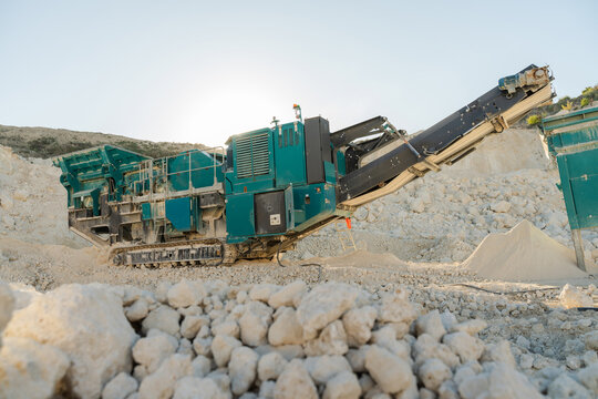 Industrial mining crusher machine at quarry site surrounded by rocks and gravel. Hard industry