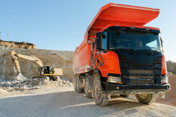 Large orange dump truck standing on quarry ground, used for hauling rocks and construction materials