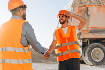 Successful smiling workers wearing orange hard hat and vests shaking hands at quarry site