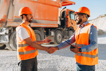 Team, smiling construction workers wearing orange hard hat and vests shaking hands at quarry site