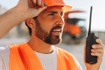 Confident, handsome male construction supervisor wearing orange hard hat communicating