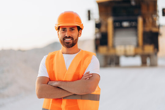 Smiling worker in orange safety vest and hard hat standing confidently with crossed arms