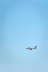 A commercial jet with red tail soaring through a vast, cloudless sky. 