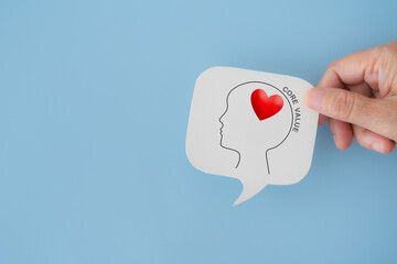 For core values, corporate values concept, hand hold real white speech bubble paper cut with head and core value symbol and text  on blue background