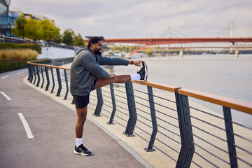 Man Stretches Leg On Riverside Boardwalk With Bridge In Background