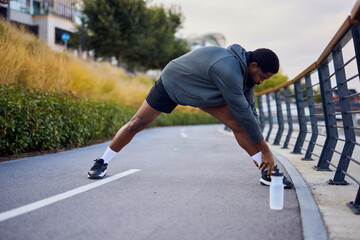 Athlete Stretches On Path By Waterfront Rail, Preparing For Morning Run Or Outdoor Workout Session