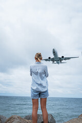 Obraz premium Young woman watching an airplane land over the sea