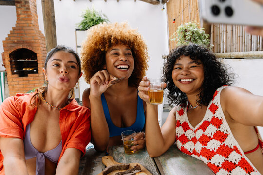 Three friends smiling and taking a selfie during Brazilian churrasco gathering