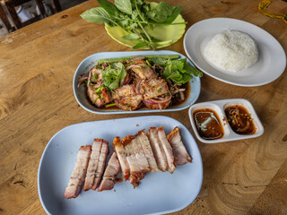 An authentic Thai feast featuring succulent crispy pork belly (Moo Krob) and a spicy grilled pork salad (Nam Tok Moo) with fresh herbs, served alongside fluffy steamed rice and traditional dipping