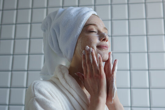 woman applies moisturizer in bathroom, soft morning routine featuring skincare in peaceful bathroom