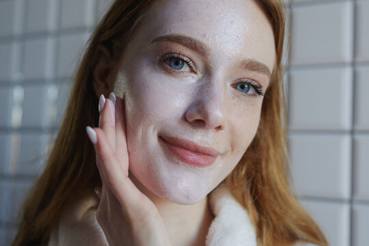 young lady moisturizes skin with care, bright morning light highlights gentle skincare application