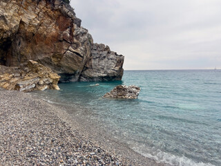 Rocky coastal shoreline with calm blue waters and overcast sky