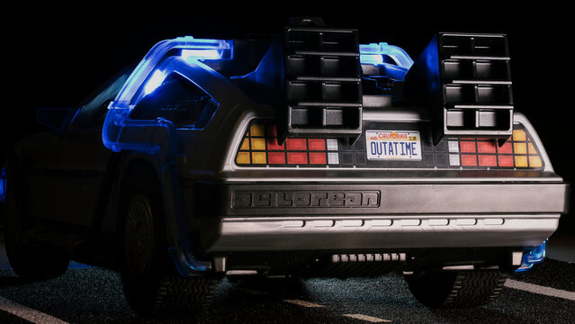 Madrid, Spain; October 25, 2025: Close-up of Playmobil DeLorean from Back to the Future, rear side illuminated in blue light on dark background, toy car on asphalt