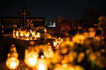 Night scene of a cemetery illuminated by hundreds of candles during All Saints Day. Warm glowing lights, bokeh and flowers creating a peaceful, spiritual atmosphere. Shot in Biały Kościół, Poland.
