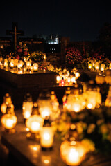 Night scene of a cemetery illuminated by hundreds of candles during All Saints Day. Warm glowing lights, bokeh and flowers creating a peaceful, spiritual atmosphere. Shot in Biały Kościół, Poland.