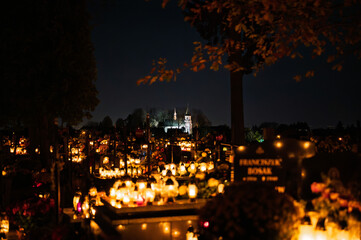 Night scene of a cemetery illuminated by hundreds of candles during All Saints Day. Warm glowing lights, bokeh and flowers creating a peaceful, spiritual atmosphere. Shot in Biały Kościół, Poland.