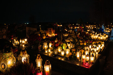 Night scene of a cemetery illuminated by hundreds of candles during All Saints Day. Warm glowing lights, bokeh and flowers creating a peaceful, spiritual atmosphere. Shot in Biały Kościół, Poland.