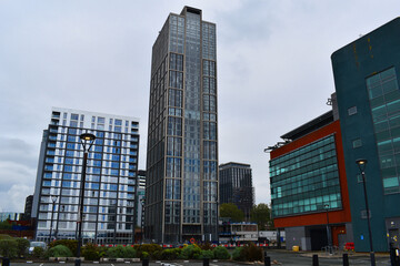 A modern cityscape view dominated by the tall, dark residential skyscraper 'The Blade' in Manchester, England. It is flanked by other contemporary high-rise residential buildings and commercial struct