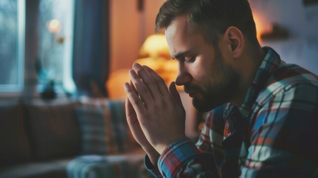 A young Caucasian man with a beard sits in a cozy living room, hands clasped in prayer. Soft lighting creates a warm atmosphere.